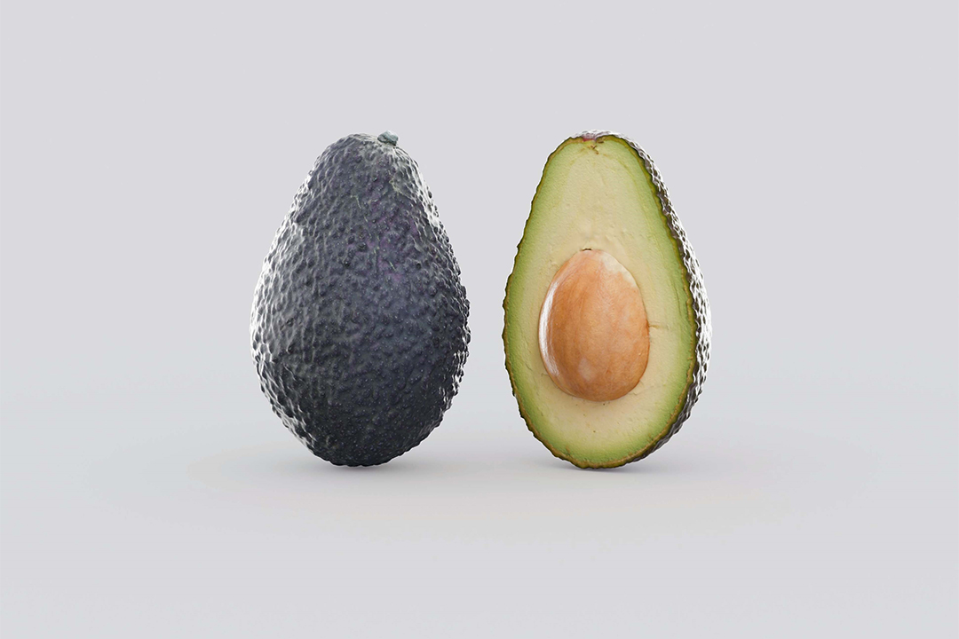 Eine ganze Avocado neben einer Hälfte einer frischen Avocado mit Kern. 