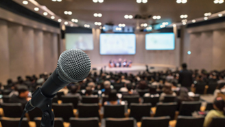 Mikrofon auf Ständer im Vordergrund, dahinter ein Konferenzsaal und Plenum