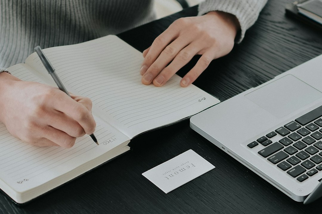 Eine Person sitzt vor dem Laptop mit Stift und Notizbuch.
