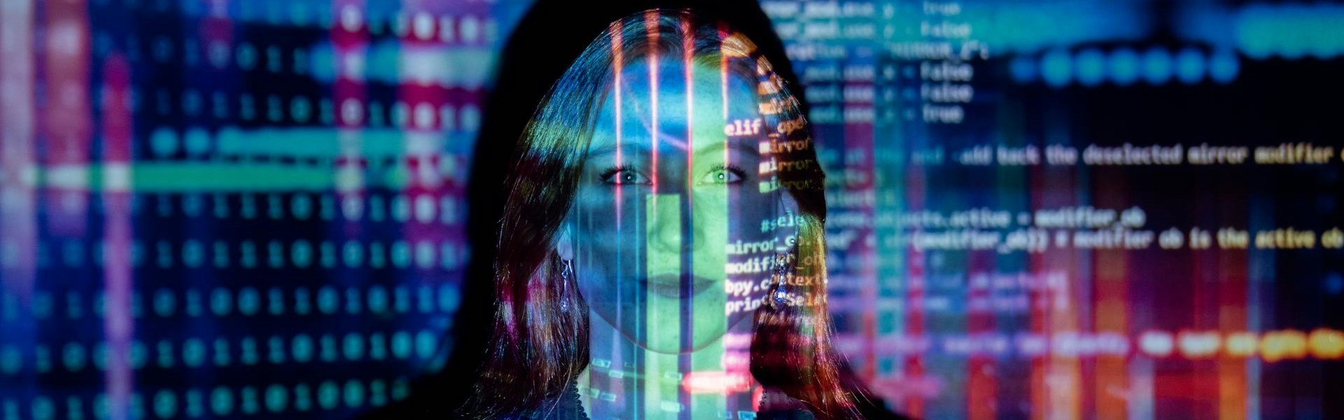 Eine Frau steht vor schwarzem Hintergrund und wird von bunten Zahlen und Code-Texten angestrahlt.