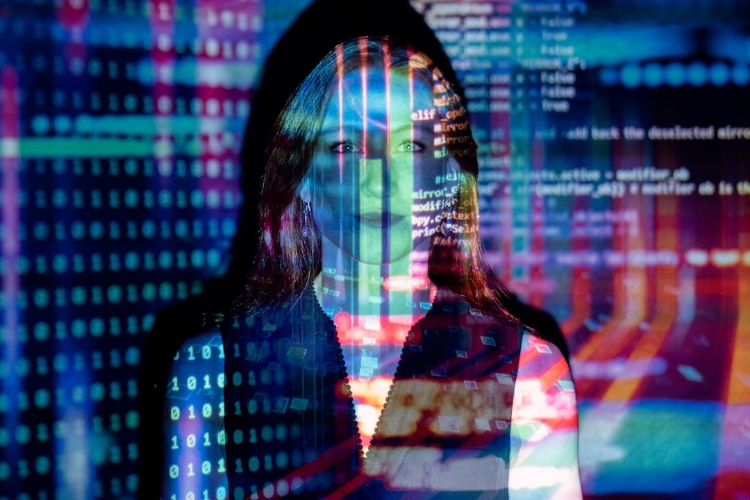 Eine Frau steht vor schwarzem Hintergrund und wird von bunten Zahlen und Code-Texten angestrahlt.