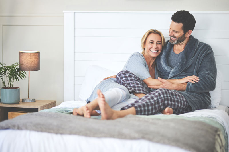 Coppia sorridente si abbraccia a letto in pigiama