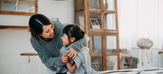 Madre sorride mentre veste la figlia in camera da letto